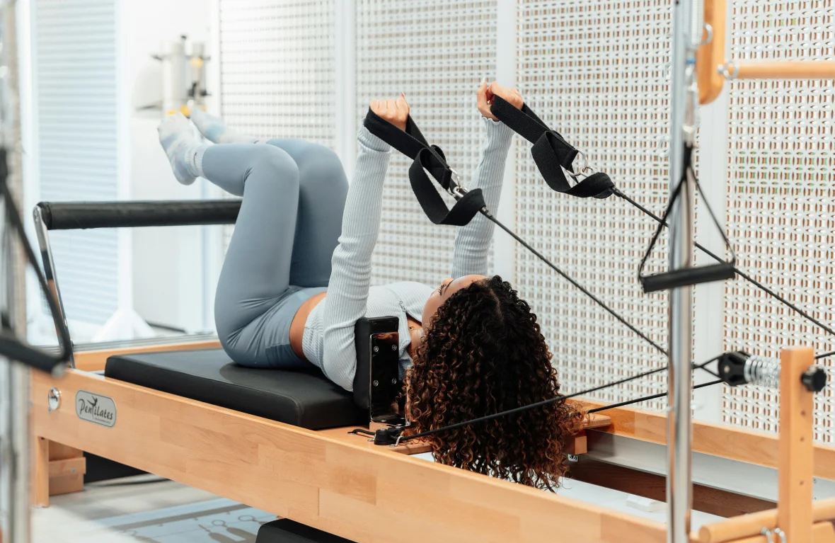 Γυναίκα εκτελεί άσκηση Clinical Pilates με φυσικοθεραπευτή σε Reformer